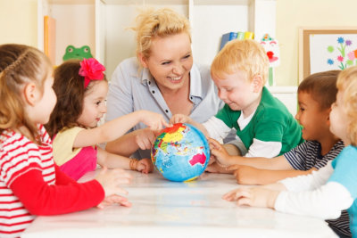 childrens hands on a globe with their teacher